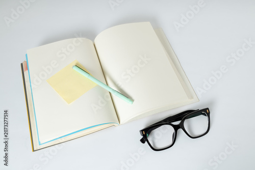 Foto Open notebook with blank sticky note, pen and eyeglasses on a clean background