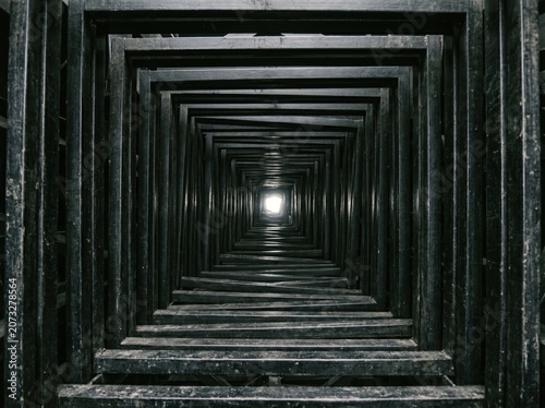 POV view through dark geometric endless tunnel towards blinking light.