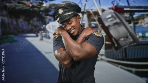 Photos Man police officer in uniform and cap with radio and badge crossing arms over chest on street near boats and pier; pride duty