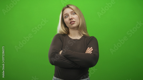 Obraz na plátně Woman in black long sleeve top with arms crossed and a clenched fist near waist, eyes closed and grimacing in green studio; annoyance dismissal