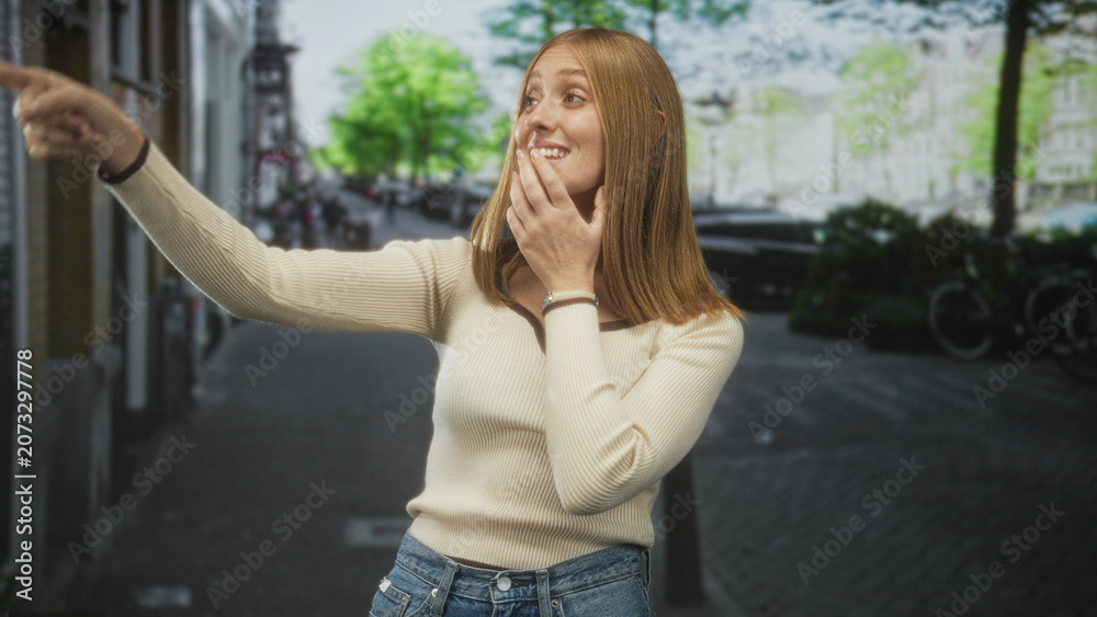 Fototapeta premium Woman points finger outward on street, hand to chin and visible pointing gesture, redhead in sweater and jeans; curiosity discovery.