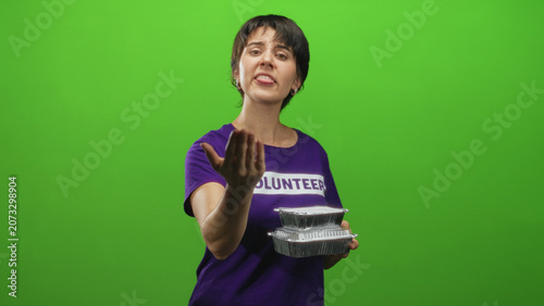 Fotografie Volunteer woman offers foil food containers and beckons with hand in studio; compassion outreach community aid