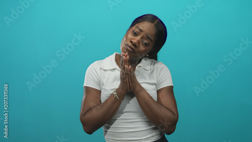 Bild auf Leinwand Woman with clasped hands pleading gesture wearing white shirt rings and bracelet in studio with turquoise backdrop; pleading apology