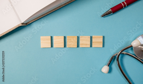 Wooden blocks arranged on blue background with pen and stethoscope