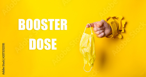 Hand Holding Yellow Mask Promoting Booster Dose Awareness Bright Background