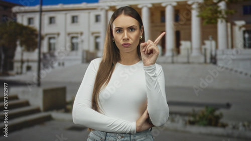 Fotografía Woman points finger with crossed arms in front of a columned building, lips pursed and stern expression; firm disapproval