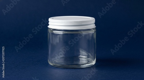 A clear glass jar with a white lid sits on a dark blue surface against a dark blue background.