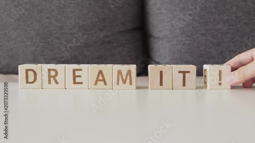 motivational phrase dream it !, laying out  by hand from letters on wooden cubes, slow motion
