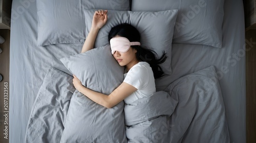 Young Asian Woman Sleeping Peacefully with Pink Eye Mask on Gray Bed Sheets Overhead View