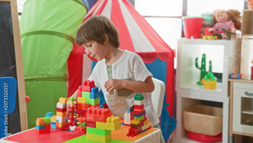Fotografía Boy stacking multicolored plastic blocks on a low play table inside building with tent and doll shelf visible; concentration