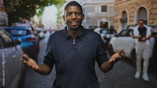 Fotografie Man showing open hands and speaking while looking aside on a busy city street with parked cars and stone buildings; curiosity conversation