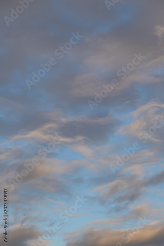 Soft pastel clouds drift across a tranquil evening sky at golden hour, casting blue and pink tones and creating a calm, dreamy atmosphere suitable for backgrounds, design and nature themes.