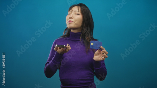 Canvas Print Woman holding smartphone and creditcard, sticking tongue out and smiling to camera in studio; playful confidence