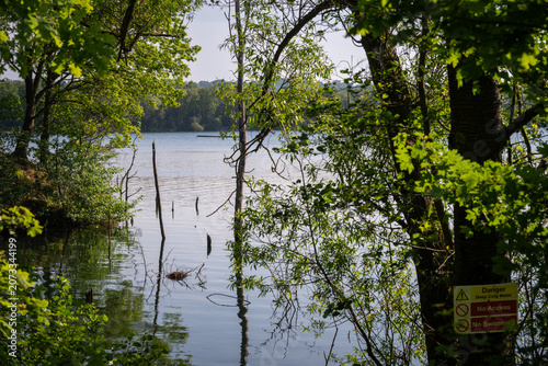 Mercers Lake near Merstham, Surrey, UK. View through trees to the cool waters of the lake. A danger sign is on a tree.