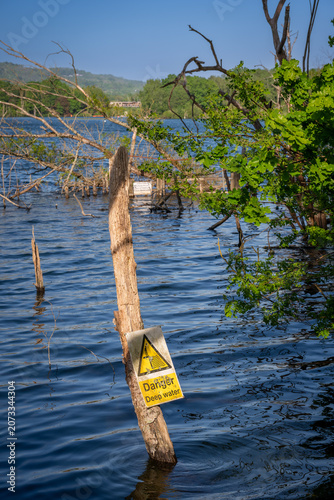 Mercers Lake near Merstham, Surrey, UK with trees on a summer's day. A danger sign warns of deep water.