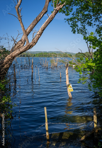 Mercers Lake near Merstham, Surrey, UK with trees on a summer's day. A danger sign warns of deep water.