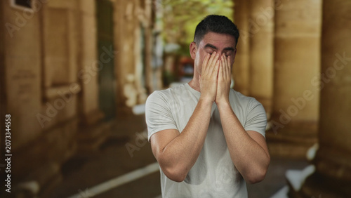 Foto Man covers face with hands on old town street, head bowed and leaning forward; sadness solitude regret