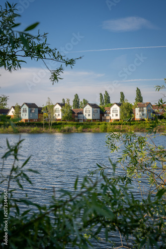 A modern housing development next to the Holmethorpe Lagoons in Mersham, Surrey, UK. Trees in the foreground. Portrait orientation.