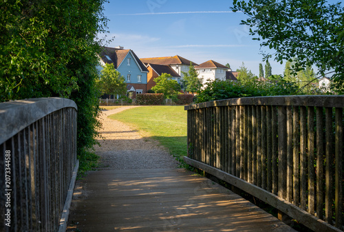 A modern housing development in Mersham, Surrey, UK. A path over a small wooden bridge leads to the houses.