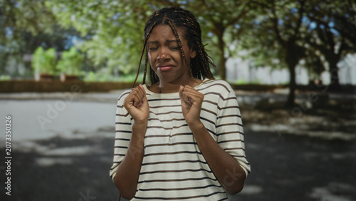 Photos Woman holding hands up with a disgusted grimace on a sunny city street near trees and pavement; disgust