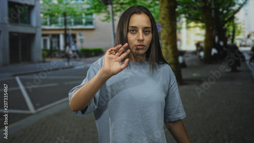 Tablou pe pânză Woman with raised palms and open hands on a city street, facing camera with a serious neutral expression; concern surrender