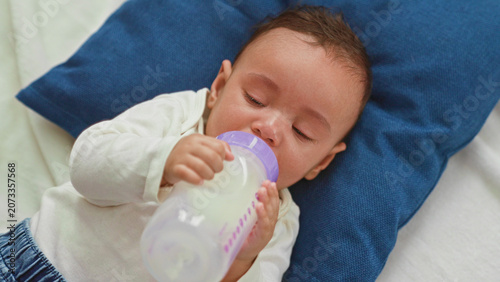 Foto Baby boy holding milk bottle and feeding while crying on bed in building; upset soothing comfort care