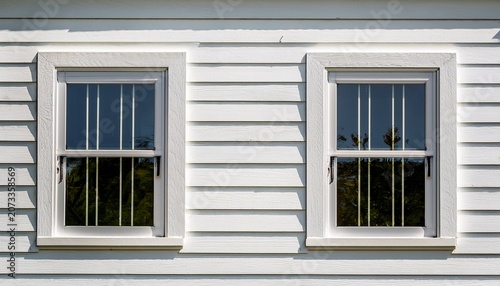 white house exterior features two windows with security bars simple window frames with white siding reflective glass panes offer privacy and clean look architectural detail
