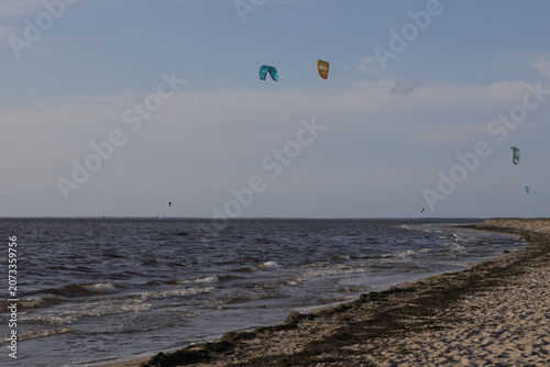 Kitesurfers on a beach with dark water and cloudy sky