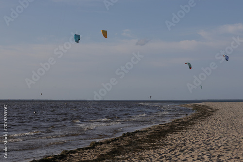 Kitesurfers on a beach with dark water and cloudy sky