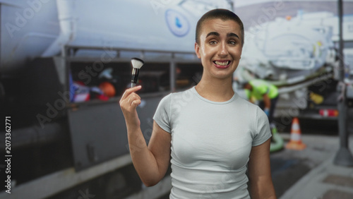 Foto Woman with short buzzed hair holding a makeup brush between fingers, hand raised and smirking by an airplane cargo door at airport tarmac; playful impatience