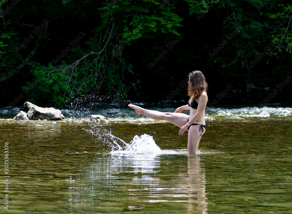 Fototapeta premium Woman splashing water playfully in a mountain river, capturing carefree summer holidays, adventure travel and refreshing natural experiences outdoors