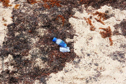 Discarded polluted plastic bottle on sandy beach.