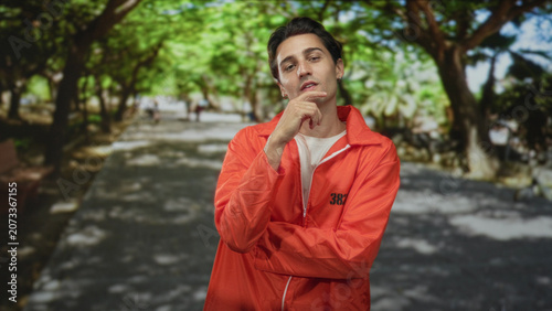 Foto Man prisoner in orange jumpsuit touching chin with hands on street while gesturing near chest; remorse solitude