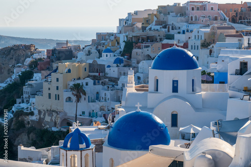 Photos Panoramic view of whitewashed buildings and iconic blue domes in Oia, Santorini, Greece, with Aegean Sea on the horizon at golden hour