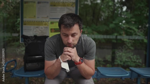 A sad, disappointed man sits at a German bus stop, checking his watch due to a delayed or cancelled public transport connection, showing frustration over transport problems and infinite waiting.