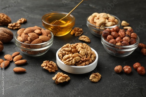 Different types of nuts in bowls and honey on dark textured table, closeup. Vegan protein snack