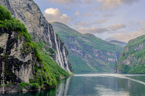 Geiranger, Majestic Norwegian Fjord Landscape, Dramatic fjord landscape with steep, green mountains and calm water under a cloudy sky. Serene natural beauty.