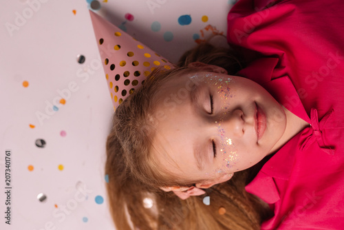 happy little girl in a birthday hat flying through confetti, top view. text space