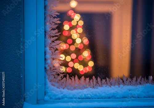 Winter frost on window pane reveals blurry warm tree lights qzkm2kpk1
