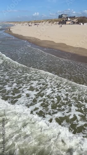 Waves roll onto wide sandy beach along North Sea coast with visitors walking on shoreline in Belgian seaside resort. Beach recreation, seaside landscape, waterfront destination