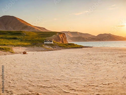 Golden light shines on a beach near a house with mountains in the background during the evening