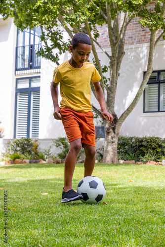 African American child in yellow t-shirt and orange shorts on front lawn controlling soccer ball