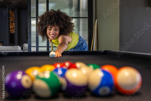 Bild auf Leinwand African American woman leaning over pool table in game room holding cue stick, w