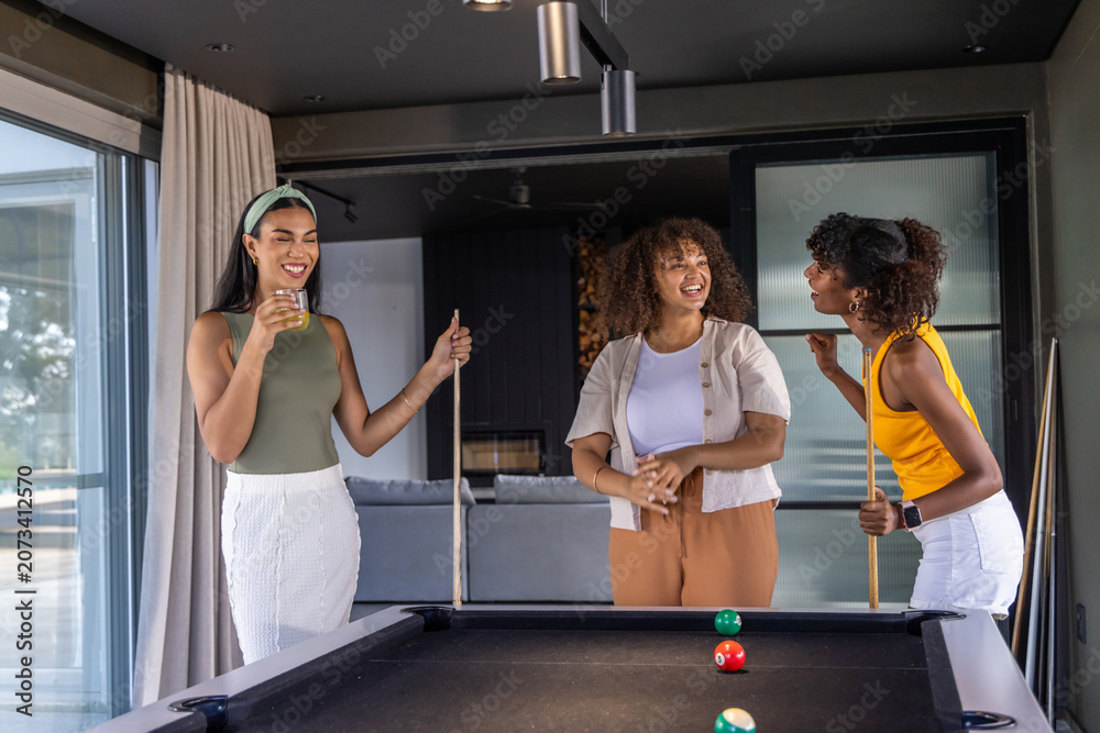 Obraz premium Diverse female friends standing around black felt pool table in modern game room holding cues