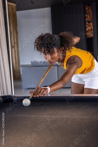 Woman lining shot, leaning over dark felt pool table at home, aiming cue and bridge hand