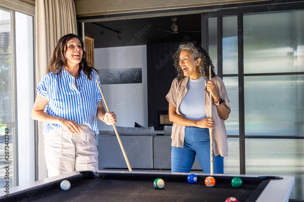 Obraz premium Diverse female friends chatting and playing on black-felt table in living room holding cues