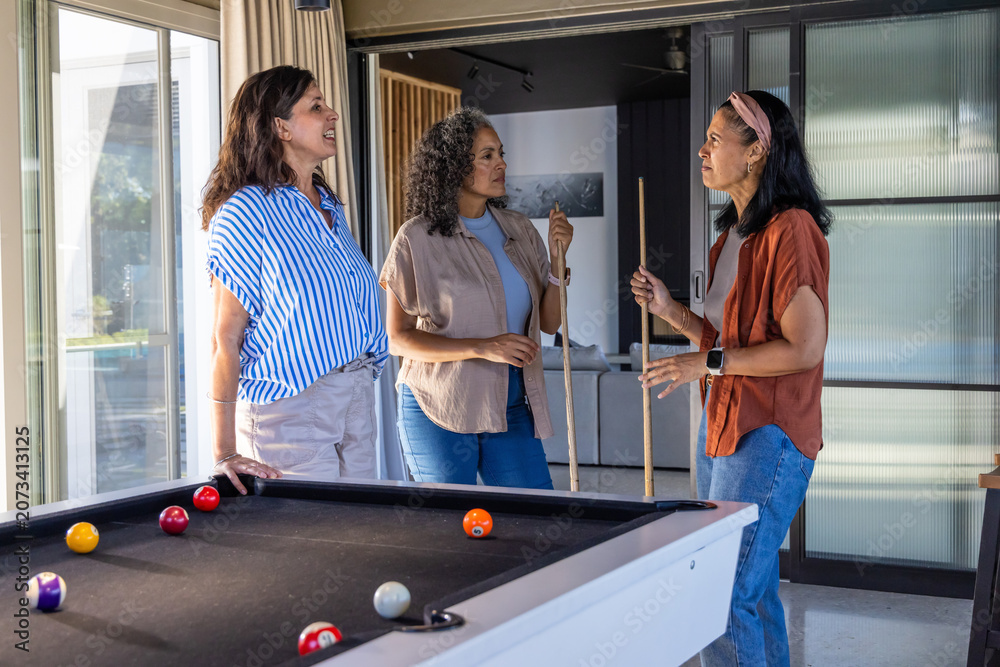 Obraz premium Diverse female friends leaning at black felt pool table holding cues planning shot in living room