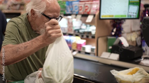 Elderly man uses credit card to pay for groceries at checkout counter in a busy grocery store filled with items