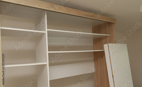 Картината върху платно Large white furniture shelves of a built-in sliding wardrobe are in the process of active installation in a room