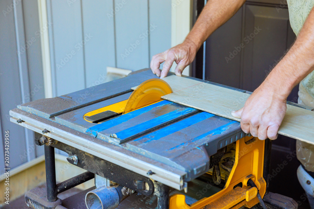 Fototapeta premium Contractor operated table saw to cut piece of wood while standing outside by house